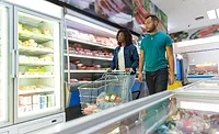 frozen-food-section couple of customers buying food together in grocery store, wheeling cart. Buyers shopping in supermarket. Choosing fresh food concept