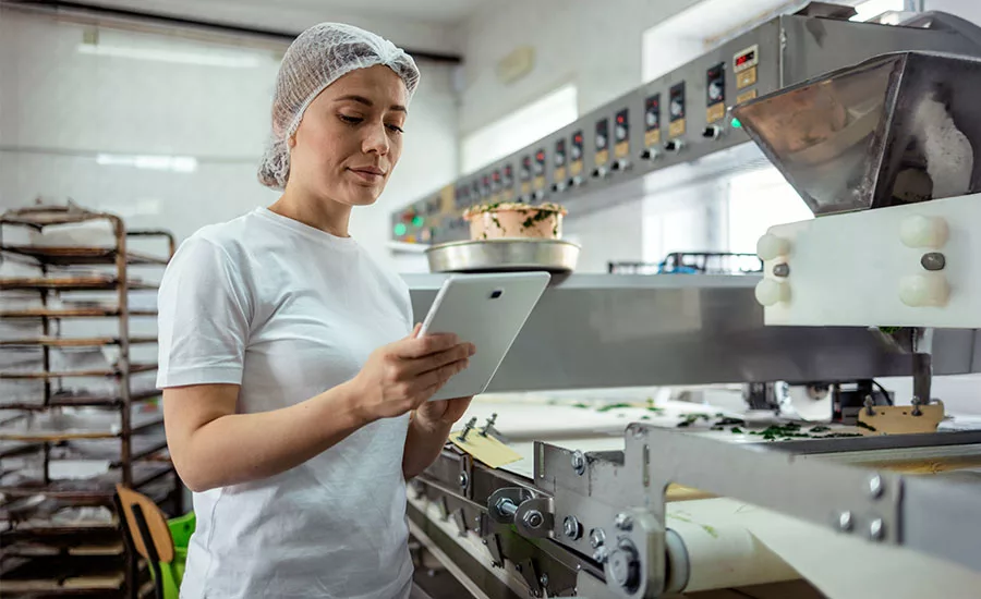 smiling woman employee with hair net using tablet in food manufacturing facility