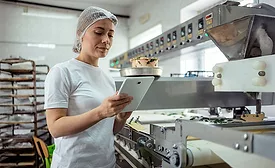 smiling woman employee with hair net using tablet in food manufacturing facility