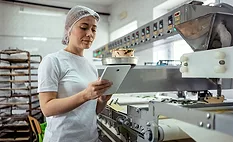 smiling woman employee with hair net using tablet in food manufacturing facility