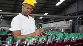 auditor with clipboard examining juice bottles in warehouse factory