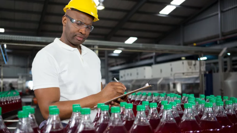 auditor with clipboard examining juice bottles in warehouse factory