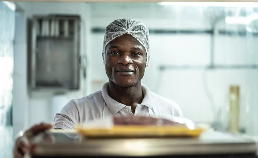 man working in food manufacturing facility wearing hairnet looking at camera with a small smile