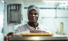 man working in food manufacturing facility wearing hairnet looking at camera with a small smile