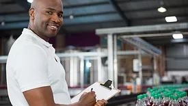 smiling man with clipboard in front of bottling line at beverage manufacturing facility