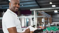 smiling man with clipboard in beverage bottling factory_wavebreakmedia_micro via Magnific.png smiling man with clipboard in front of bottling line at beverage manufacturing facility