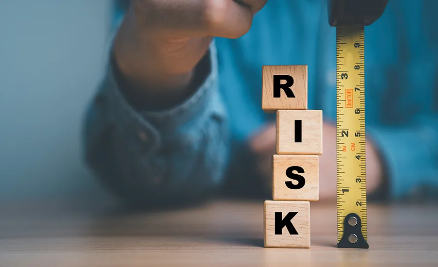 person holding tape measure next to stack of block letters that say R I S K. measuring risk concept
