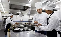 chefs in a professional kitchen setting, appearing to be discussing or reviewing something on a digital tablet. chefs in a professional kitchen setting, appearing to be discussing or reviewing something on a digital tablet.