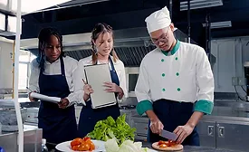 three chefs, one of them is slicing vegetables