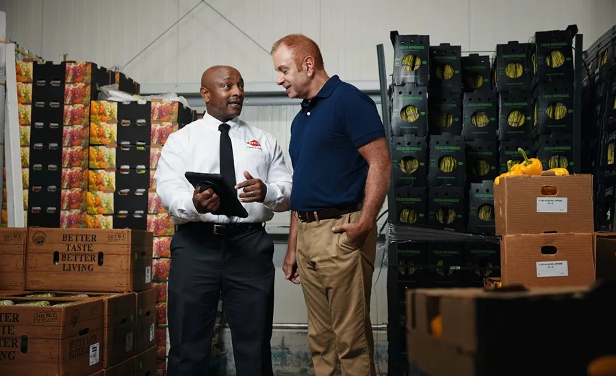 Two men standing in a produce storage facility having a discussion.