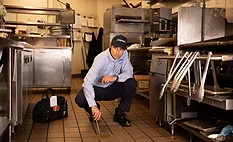a person performing equipment maintenance, specifically cleaning the floor in a commercial kitchen. 