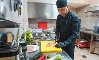 The image shows a person working on food preparation, likely in a commercial kitchen setting.