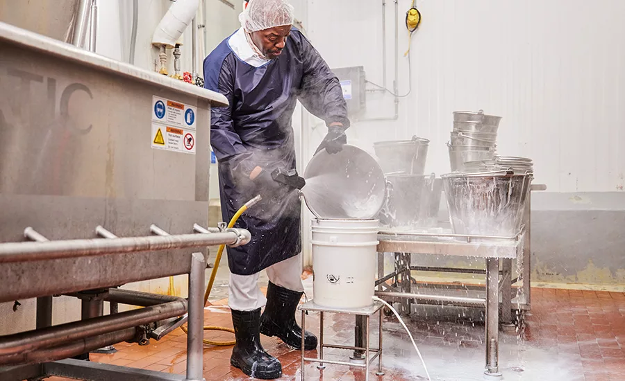 This image depicts a worker cleaning stainless steel machinery in a food processing plant