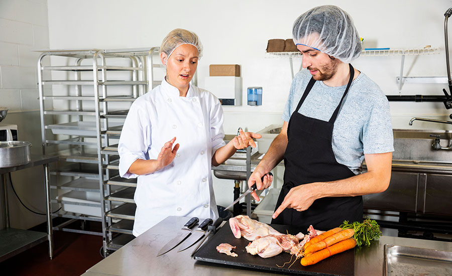 a workplace food safety violation where raw poultry and fresh carrots are placed on the same cutting board, creating a risk of cross-contamination