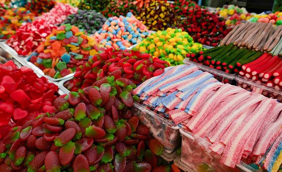 This image displays a vibrant assortment of colorful gummy candies and sugary treats arranged on a market stand. 