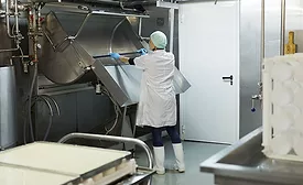 The image shows a worker cleaning a industrial cheesemaking curdling tank within a dairy factory. 