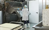 The image shows a worker cleaning a industrial cheesemaking curdling tank within a dairy factory. 