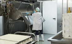 The image shows a worker cleaning a industrial cheesemaking curdling tank within a dairy factory. 