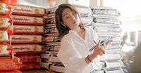 This image shows a woman, possibly the owner of an organic rice wholesale store, working amidst stacks of rice bags. This image shows a woman, possibly the owner of an organic rice wholesale store, working amidst stacks of rice bags.