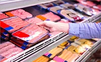 The image displays a person selecting packaged fresh chicken meat from a supermarket display cooler. The image displays a person selecting packaged fresh chicken meat from a supermarket display cooler.