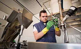 This image depicts a professional mechanic working on a piece of stainless steel processing machinery in a factory setting. 