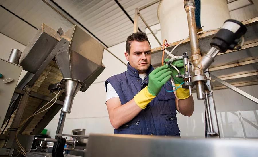 This image depicts a professional mechanic working on a piece of stainless steel processing machinery in a factory setting. 