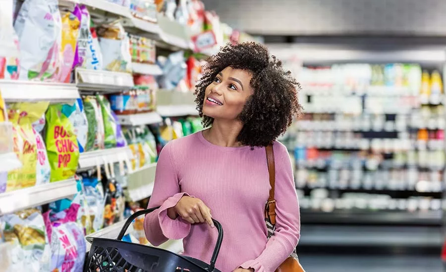 a person looking at items on a grocery store shelf while holding a black shopping basket.