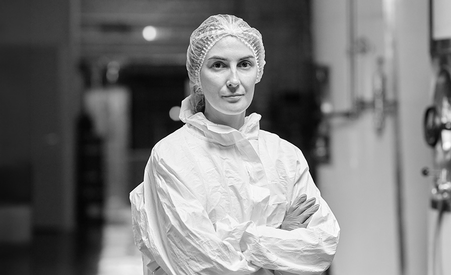 a female process technician or industrial worker wearing a white protective coverall suit and a hairnet