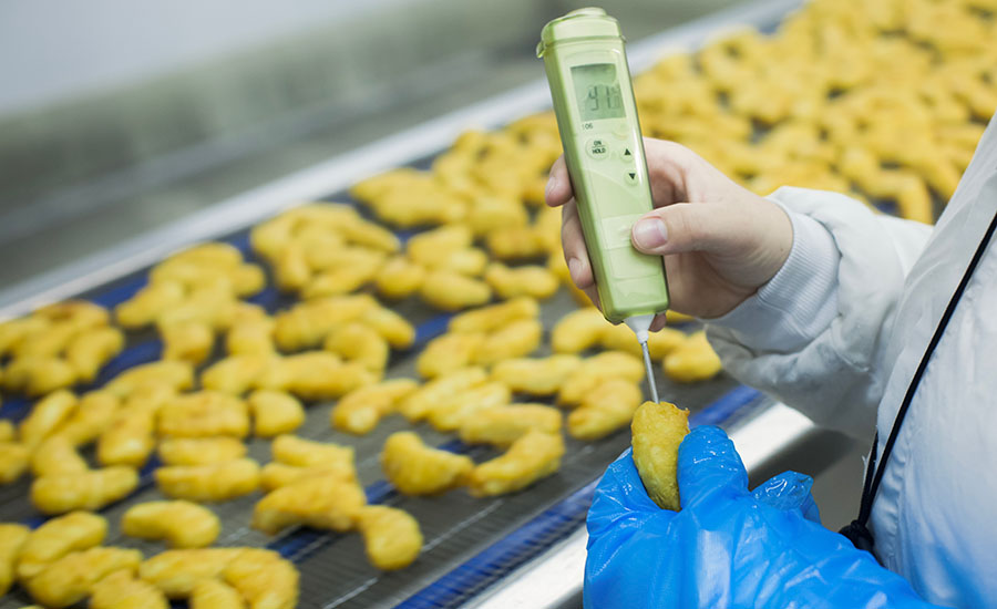 a food quality control worker wearing blue gloves and protective gear while using a handheld digital temperature probe or testing device