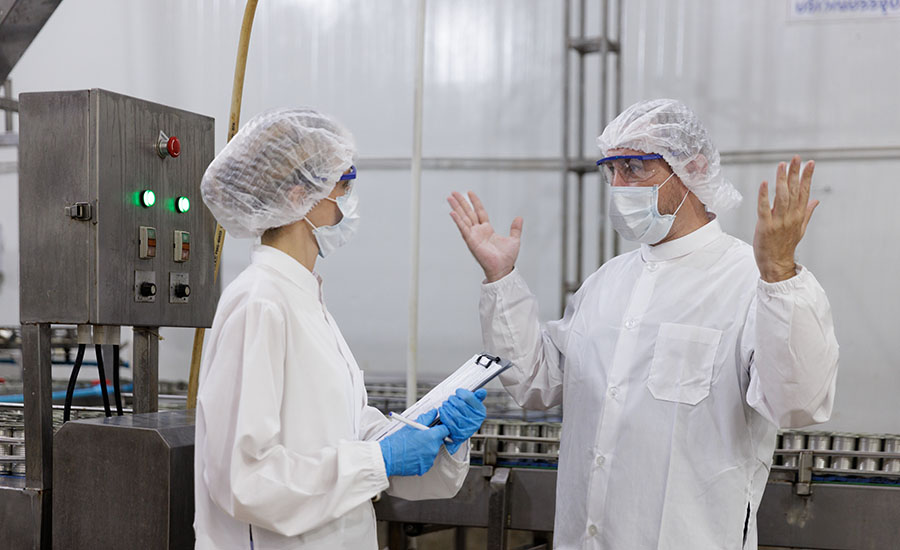 two quality control inspectors wearing protective lab coats, hairnets, and face masks