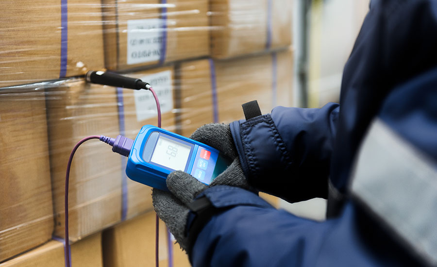a worker using a digital thermometer and probe to check the temperature of boxed goods in a cold storage or cold chain environment