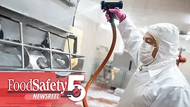 a sanitation worker in protective gear using a high-pressure washdown hose to clean industrial food processing equipment