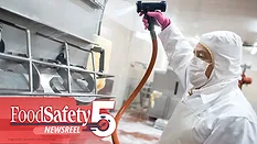 a sanitation worker in protective gear using a high-pressure washdown hose to clean industrial food processing equipment