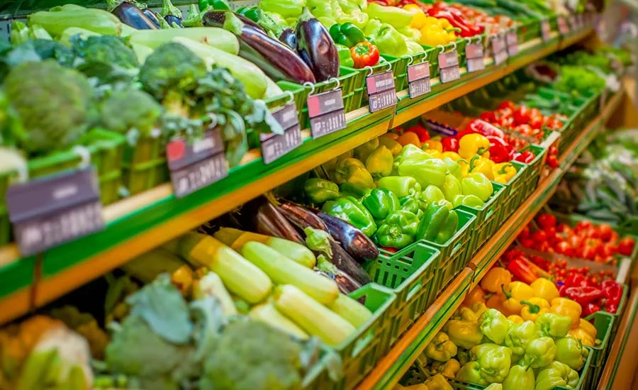 grocery store shelf display stocked with fresh vegetables like broccoli, zucchini, eggplant, and colorful peppers