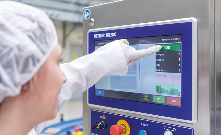 an operator in cleanroom gear interacting with a Mettler Toledo x-ray inspection system touchscreen interface on a production line
