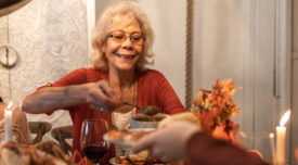 an older smiling woman serving herself food at a dinner table