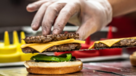 gloved hand assembling cheeseburger