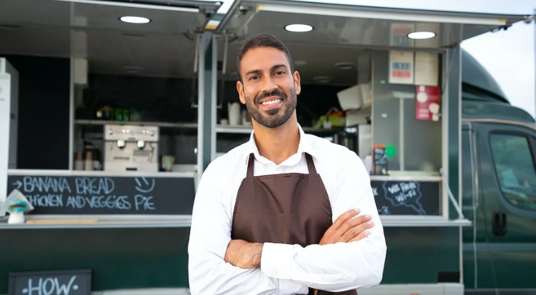 man in an apron smiling in front of a food truck