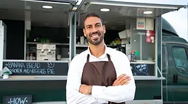 man in an apron smiling in front of a food truck