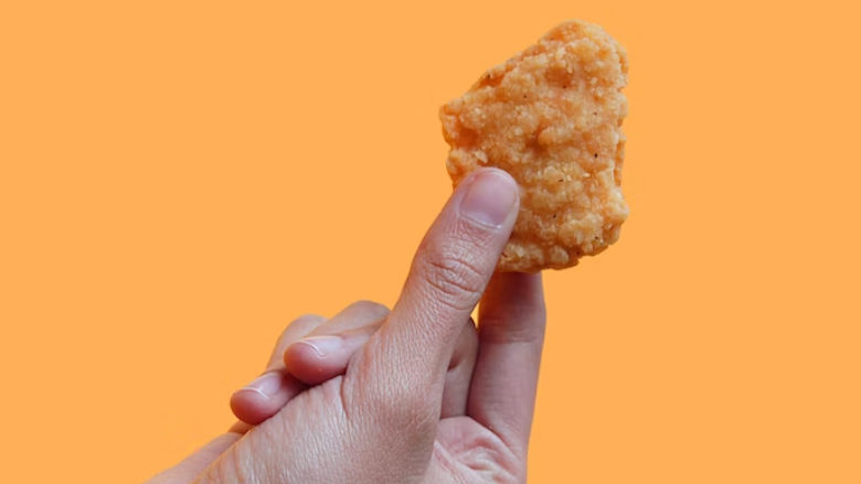 person holding a chicken nugget against a yellow background