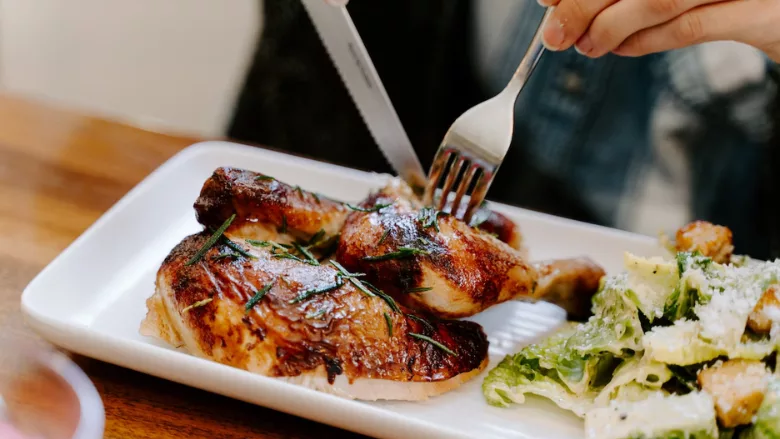 someone eating grilled chicken wing with fork and knife