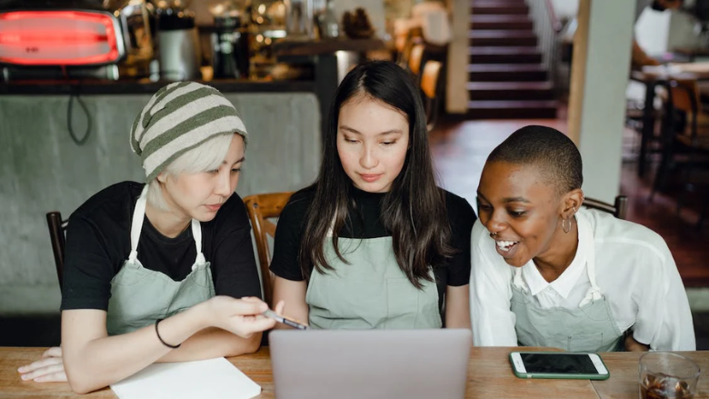 three waitresses working on a laptop in a cafe