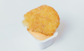 fast food nugget dunked in a mayonnaise-based condiment in a plastic container