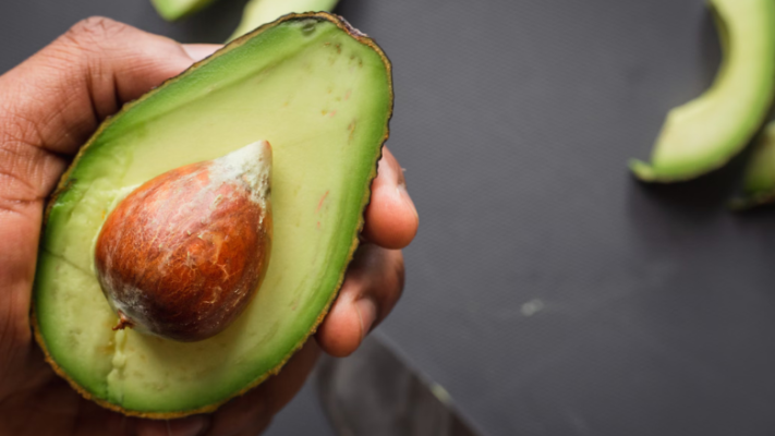 a hand holding half an avocado with pit inside