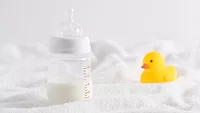 half full baby bottle next to rubber duckie on white surface half full baby bottle next to rubber duckie on white surface