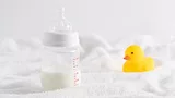 half full baby bottle next to rubber duckie on white surface half full baby bottle next to rubber duckie on white surface