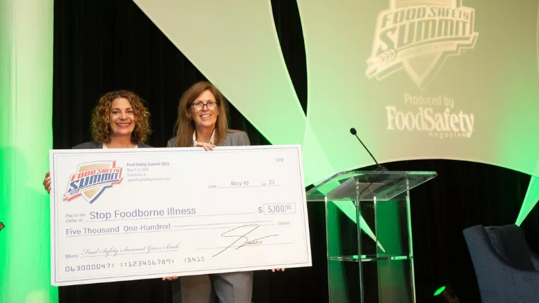 mitzi baum and stacy atchison holding giant donation check at 2023 food safety summit gives back networking reception