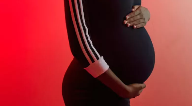 pregnant belly in a black dress against a red background
