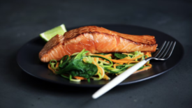 salmon filet and greens on black plate black background