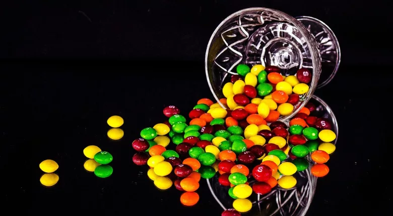 skittles tumbling out of a glass bowl tipped on its side